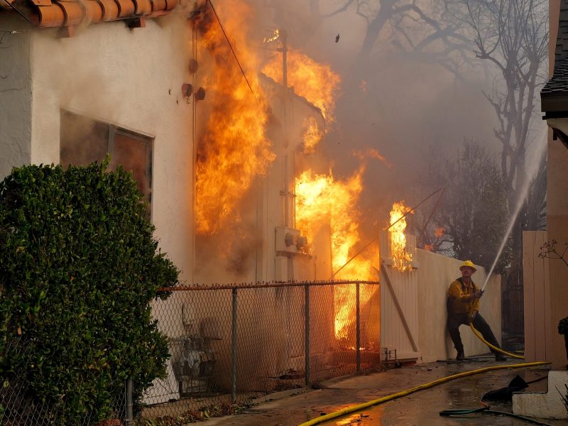 A firefighter sprays water on a house to protect it from the Eaton Fire in the Altadena neighborhood on January 08, 2025. Photo by Nick Ut/Getty Images